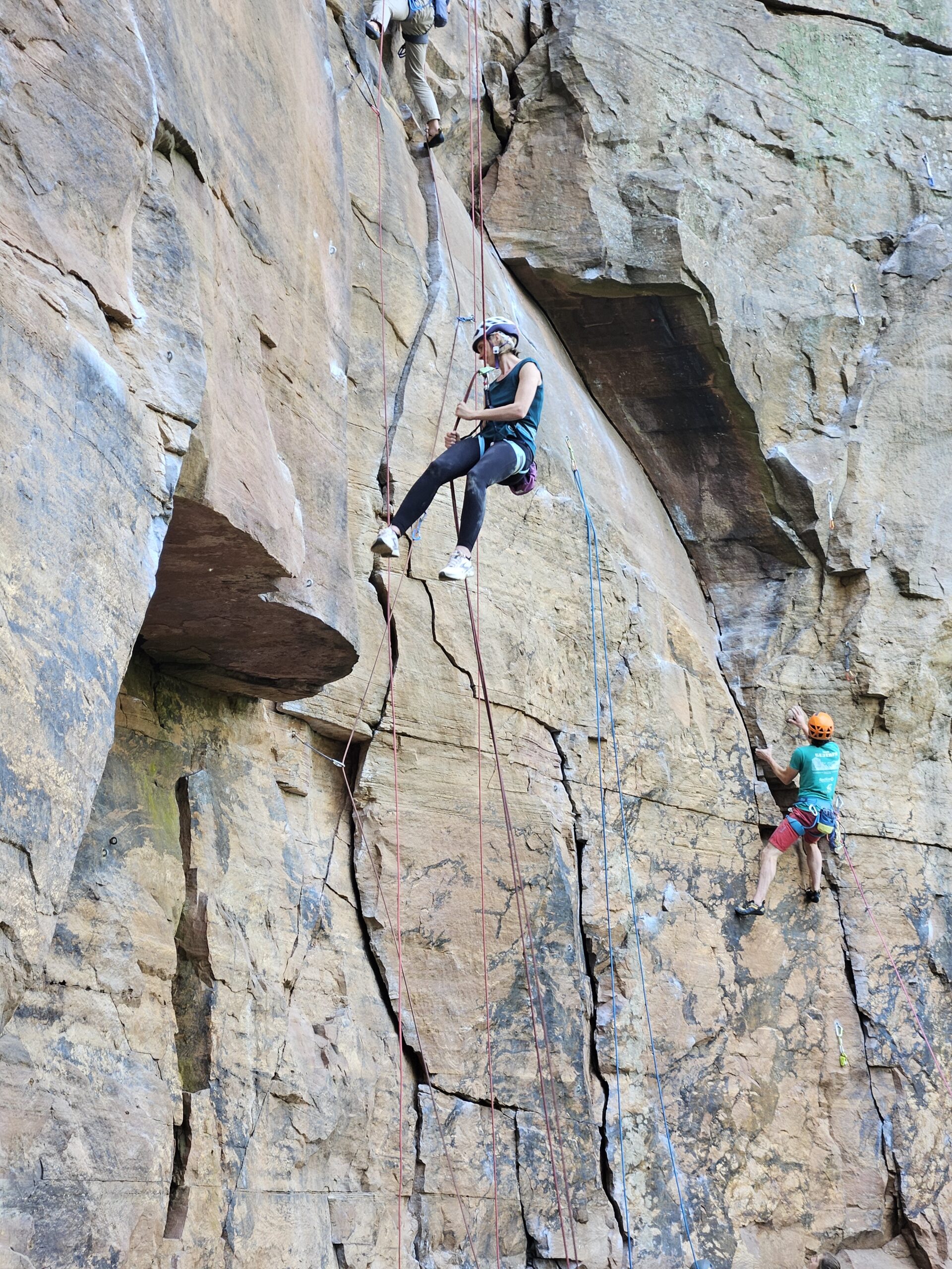 Une grimpeuse casquée descend sur corde devant la falaise